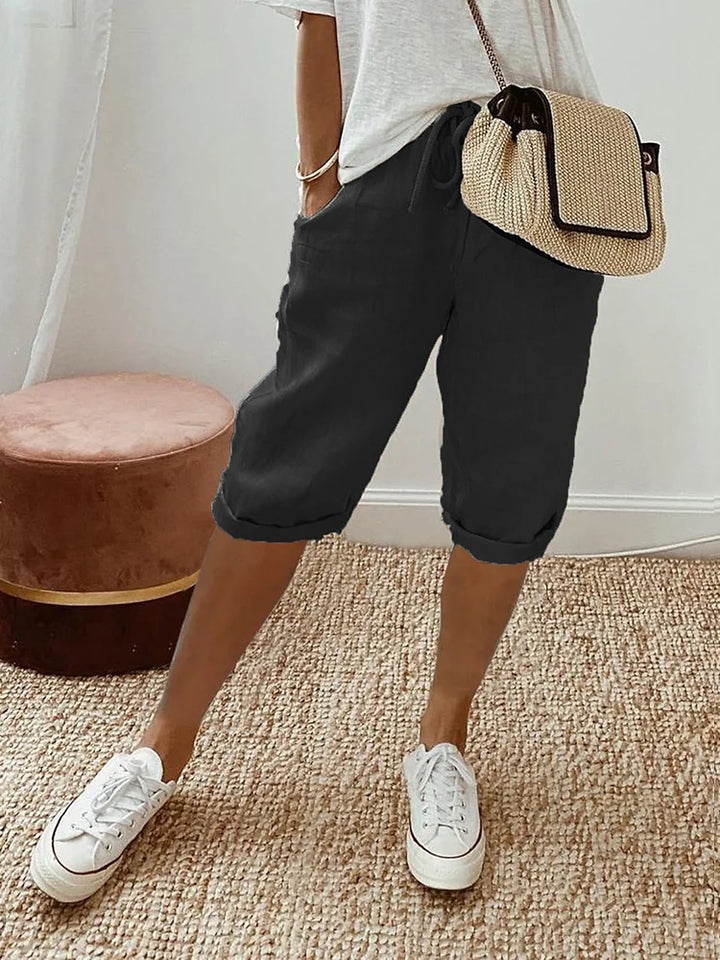 Black comfort shorts matched with a white top and sneakers, showcased in a comfortable indoor room with woven rug and stool.