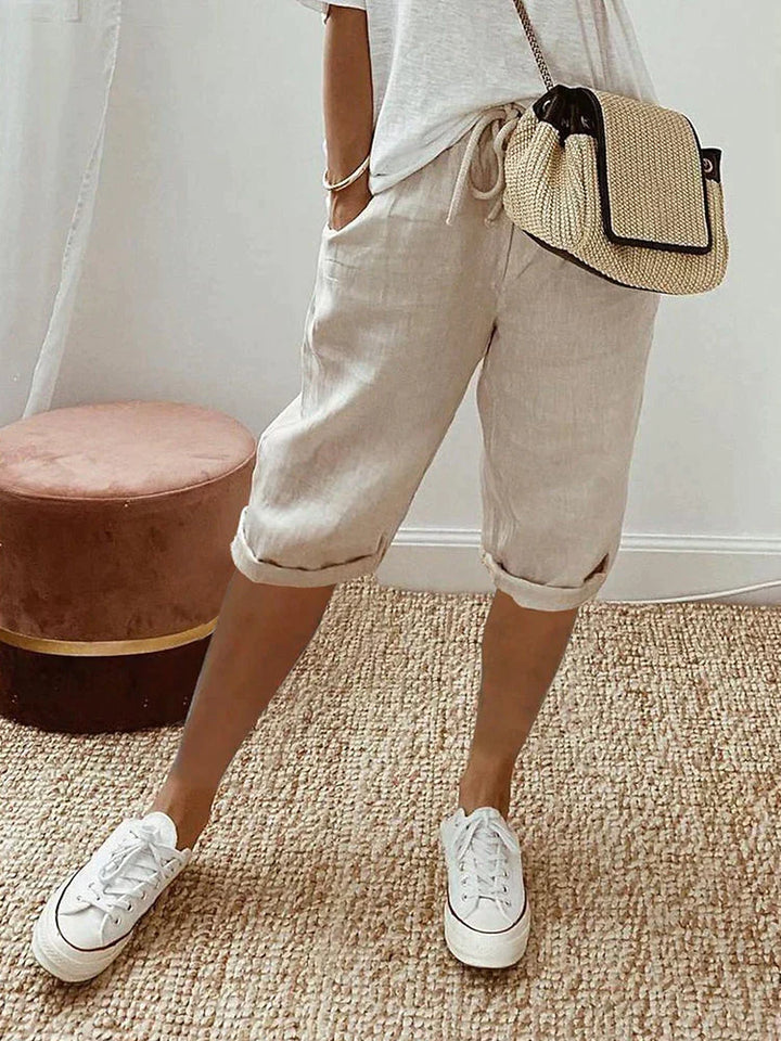 Beige comfort shorts worn with a white top and sneakers, featured in a warm indoor setting with a woven rug and cushioned stool.