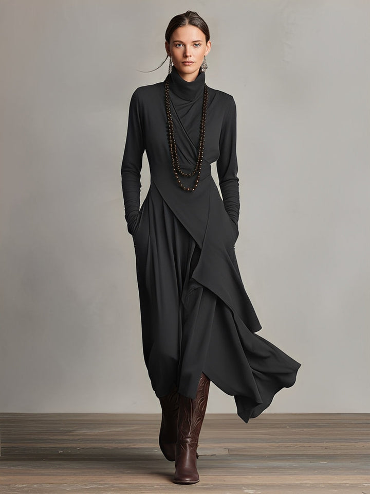 Woman in a black stretch maxi dress with long sleeves and flowing layers, wearing long necklace, in a studio setting.