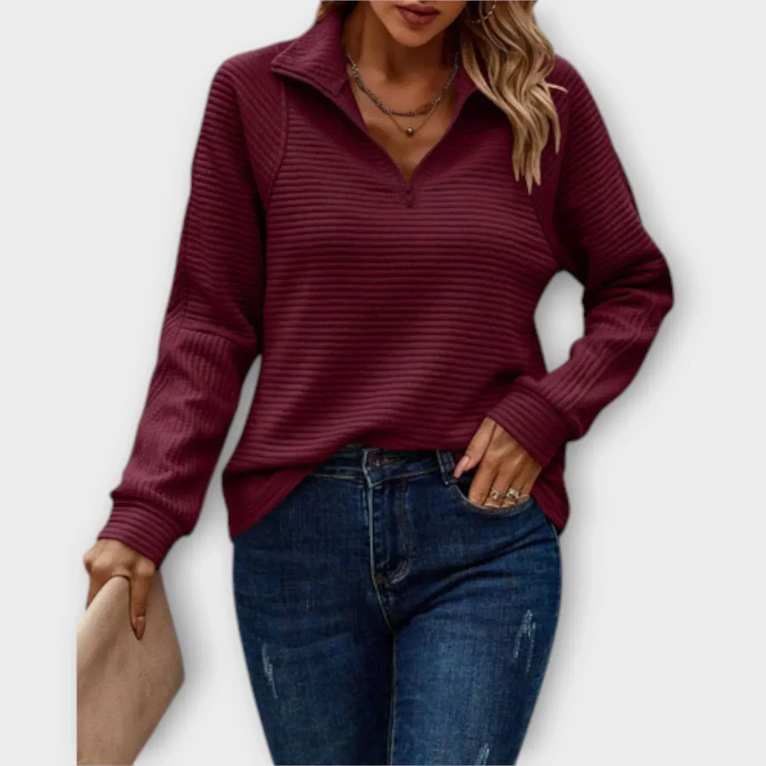 Woman wearing a burgundy ribbed half-zip pullover with jeans, holding a clutch, against a plain background.