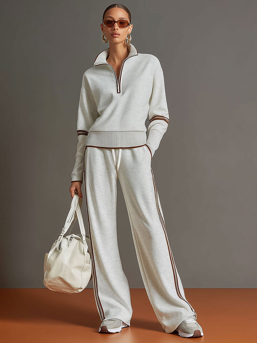Effortless matching lounge set in light gray with contrast stripes, styled with white sneakers and a bag in a studio setting.