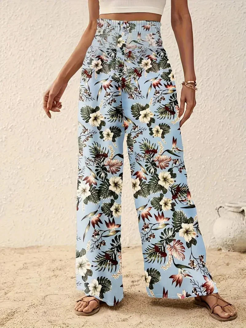 Close-up of light blue floral trousers with red and green patterns, on a sand-covered floor.