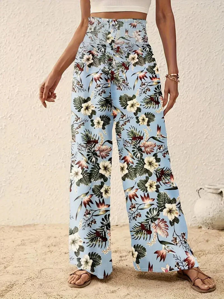 Close-up of light blue floral trousers with red and green patterns, on a sand-covered floor.