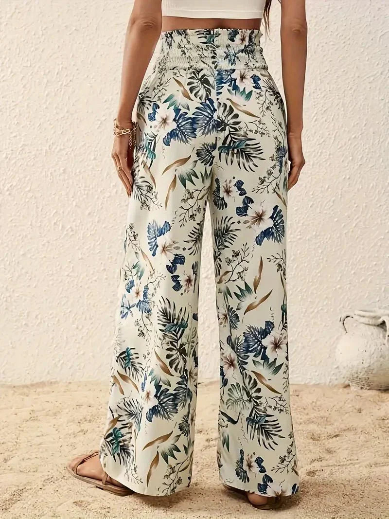 Back view of floral trousers in blue and green tones with a beachy, sand-strewn setting.