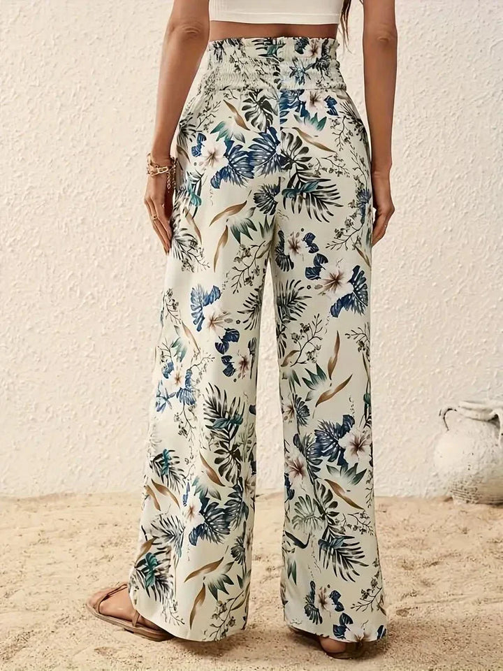 Back view of floral trousers in blue and green tones with a beachy, sand-strewn setting.