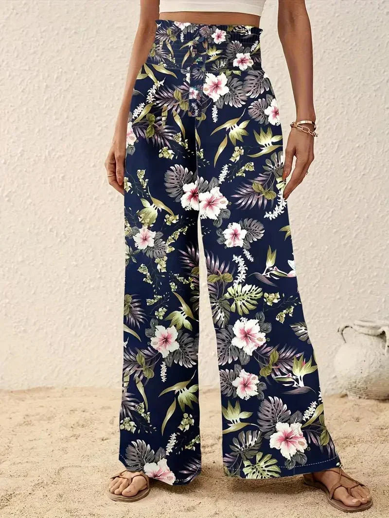 Close-up of dark floral trousers with vibrant pink and green flowers, displayed on a sandy floor.
