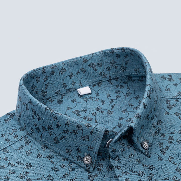 Close-up of blue floral shirt collar with dark patterns, studio background.