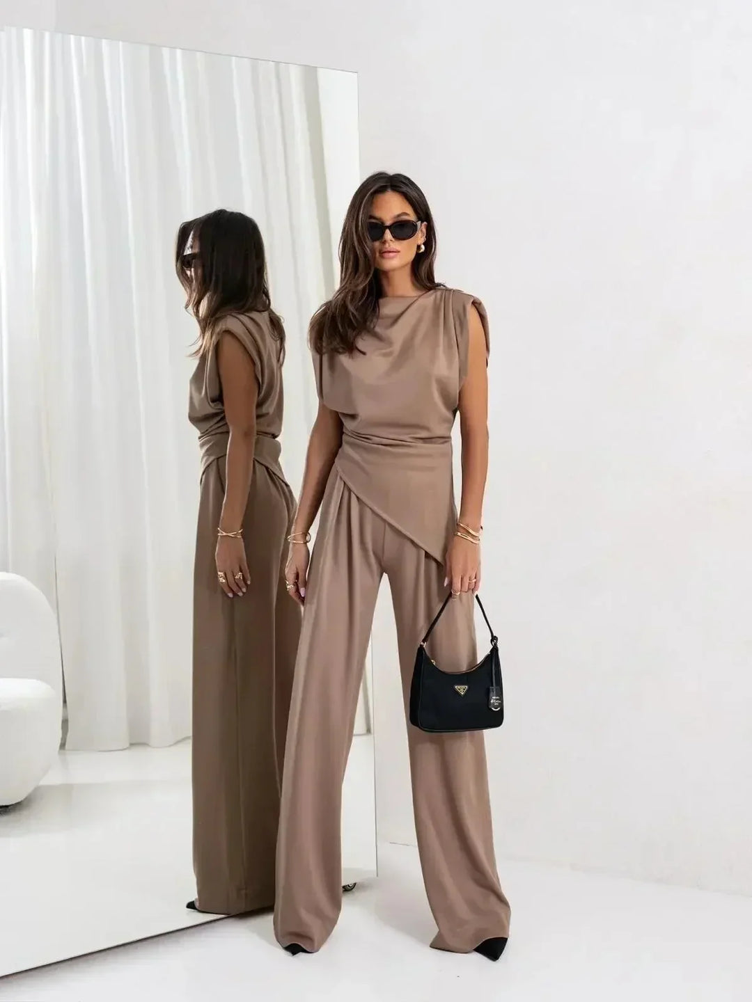 Sophisticated taupe two-piece set with an asymmetrical top and wide pants, posed in front of a large mirror in a modern room.