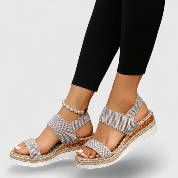 Gray orthopedic sandals with textured straps and platform soles, paired with black leggings and a pearl anklet in a studio.