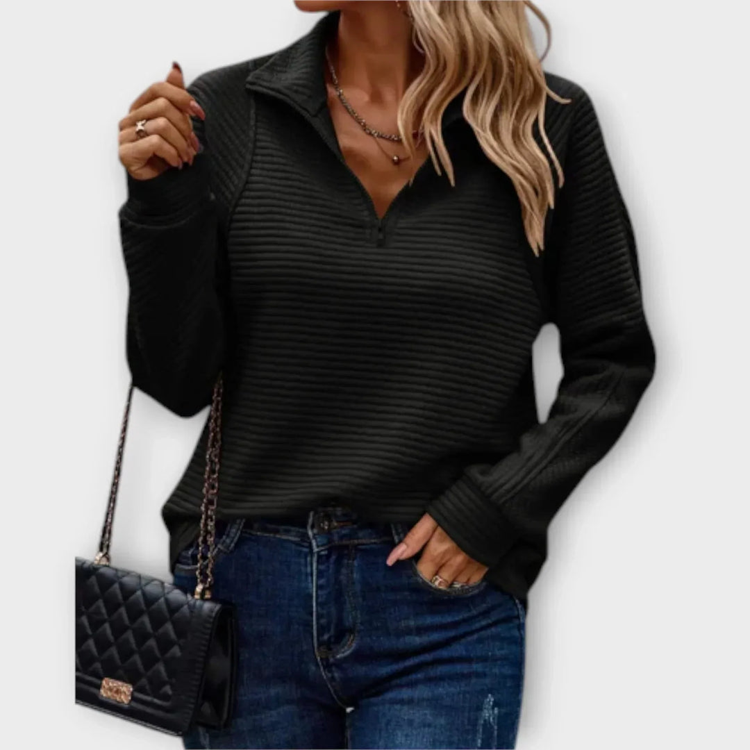 Woman in a black ribbed half-zip pullover, carrying a black quilted purse, paired with jeans, in front of a plain background.