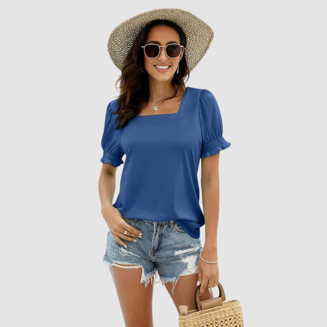 Woman in blue square neck top, denim shorts, straw hat, sunglasses, holding woven bag, studio environment.