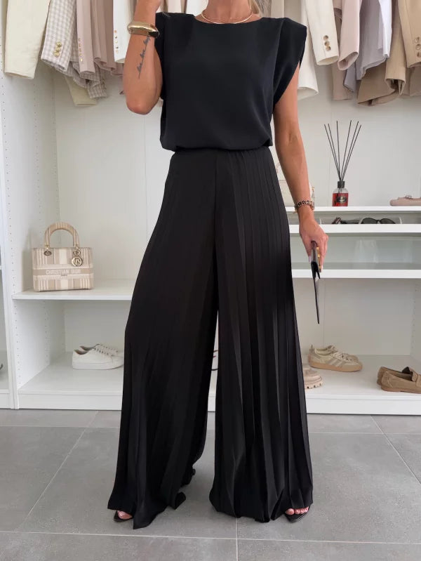 Close-up of woman in a black two-piece set, featuring a structured sleeveless top and wide-leg pants, in a closet setting.