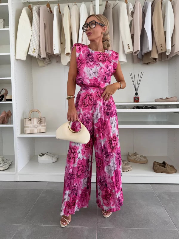 Woman modeling a vibrant pink floral two-piece outfit with wide-leg pants and short-sleeve top, in a stylish wardrobe room.