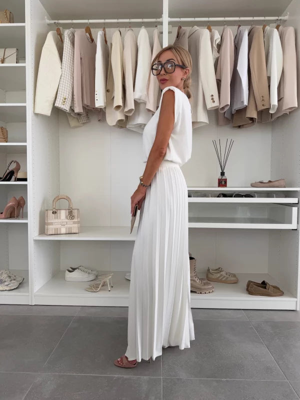 Side view of woman wearing an elegant white two-piece set, featuring a flowy top and wide-leg pants, in a modern closet.