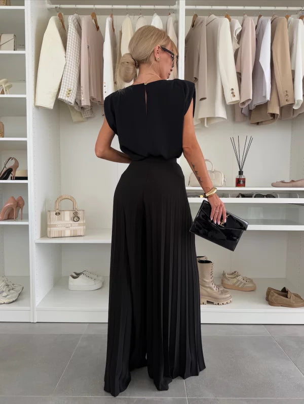 Back view of woman wearing a black two-piece set with flowy wide-leg pants, standing in a stylish wardrobe room.