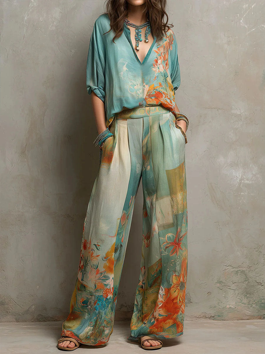 Woman wearing a flowing teal and orange floral-patterned blouse and pants set, standing against a textured wall.