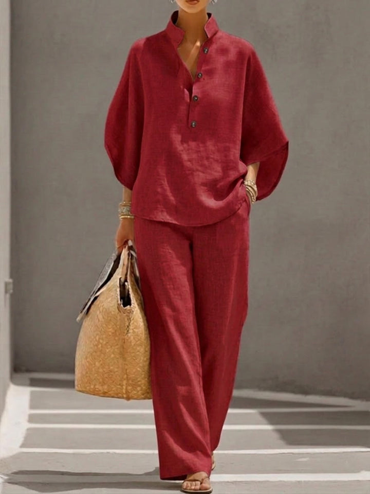 Woman wearing a red two-piece set with a high collar and buttons, carrying a woven bag, walking in a minimalist urban setting.