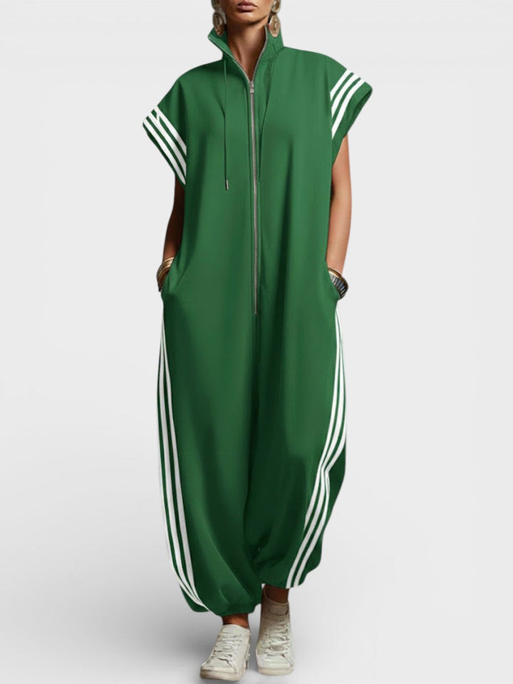 Model wearing green zip neck jumpsuit with white side stripes and cap sleeves, studio background.