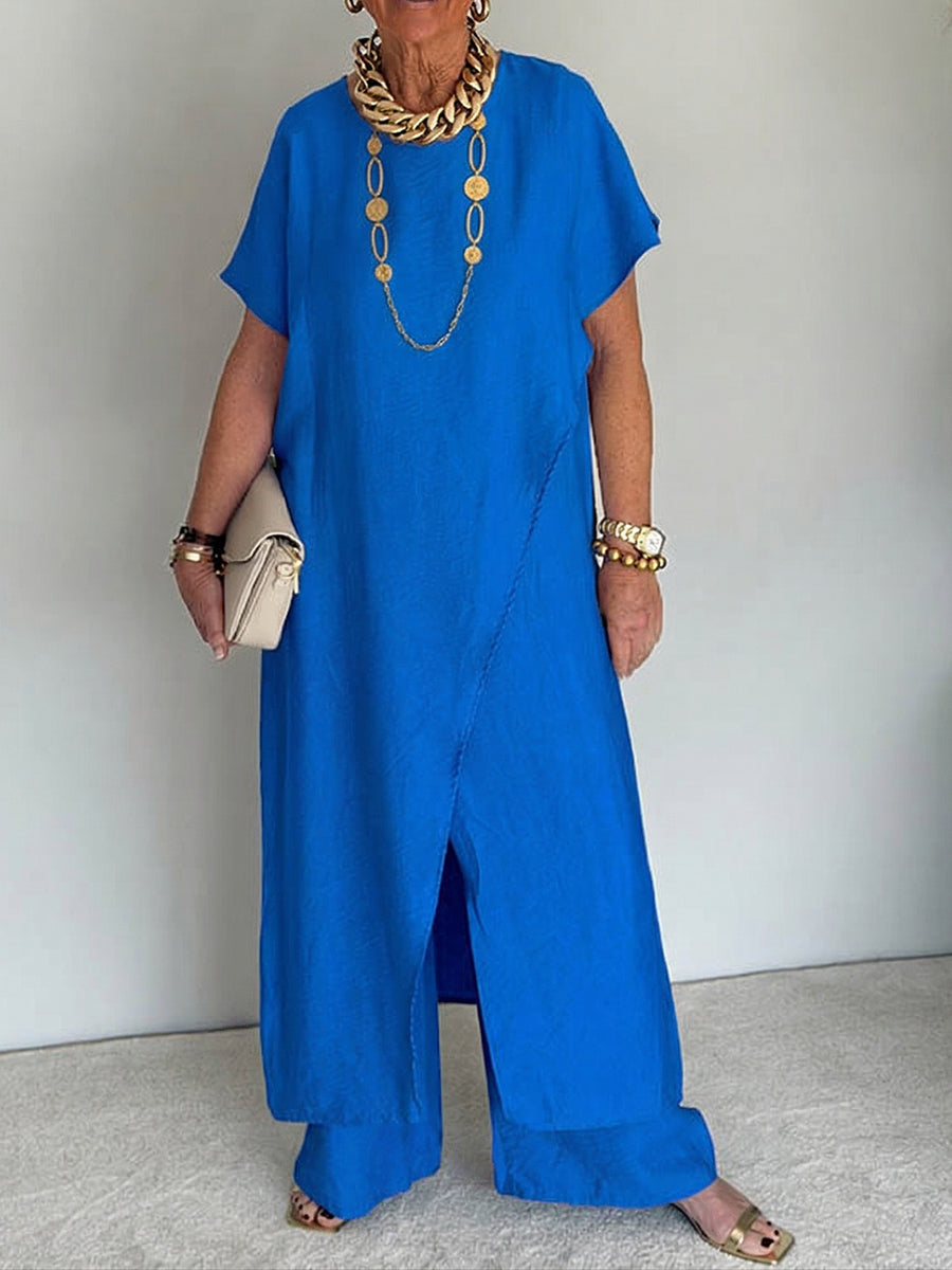 Person wearing a bright blue flowing set with short sleeves and wide-leg pants, accessorized with gold jewelry and holding a beige clutch in a studio setting.