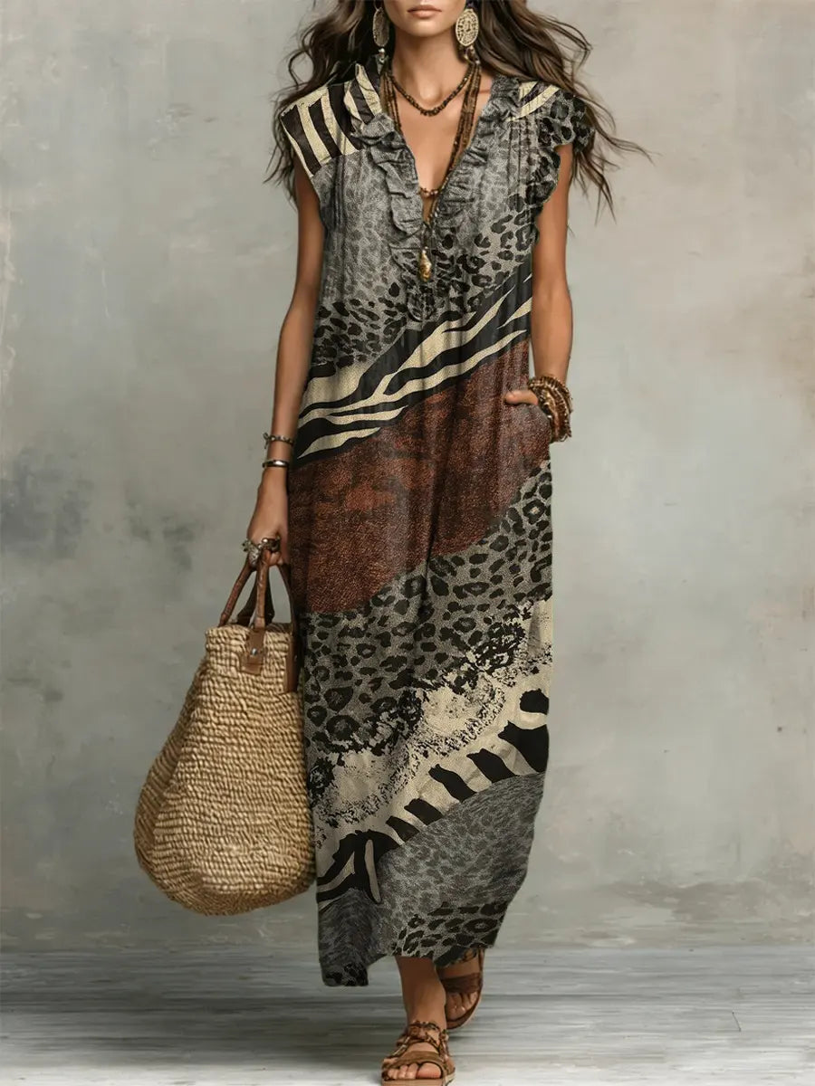 Model in flowing mixed print maxi dress with ruffled collar in studio setting, holding a woven bag.