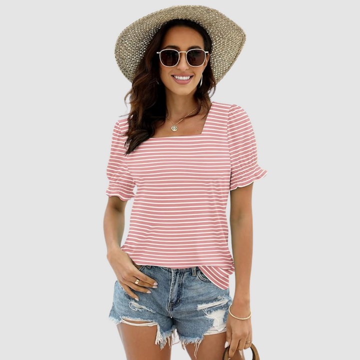 Woman wearing pink-striped top, denim shorts, straw hat, holding woven bag. Studio background.