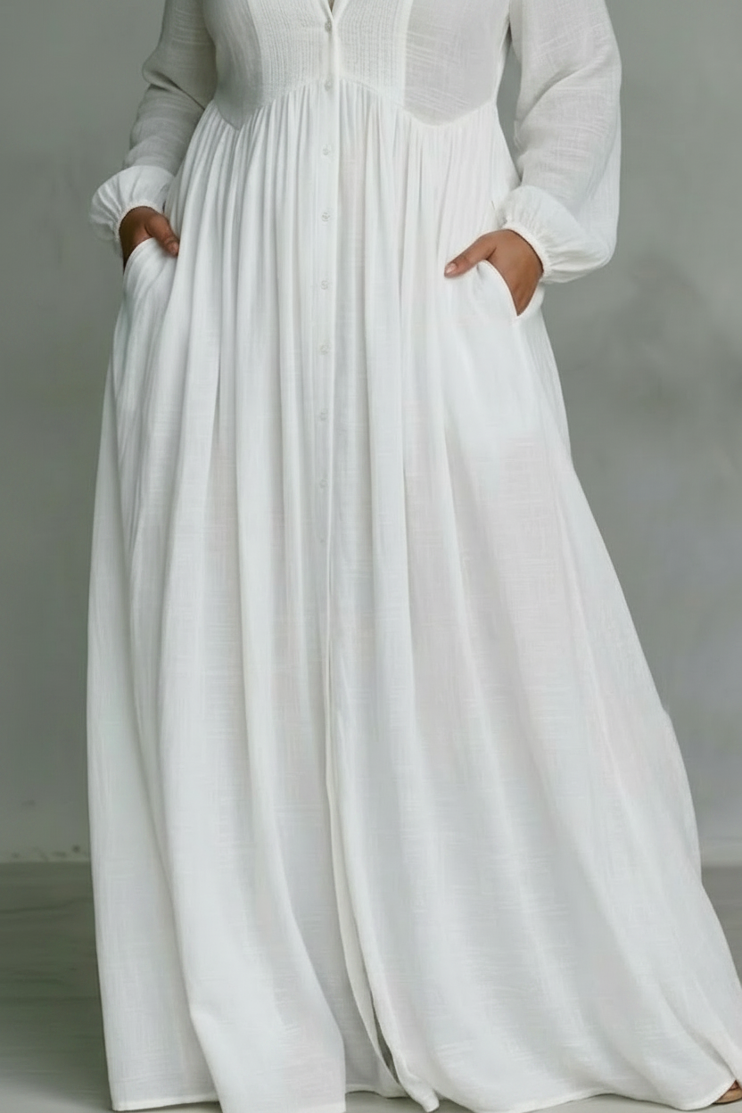 Close-up of the lower half of a white flowing maxi dress with pockets in a studio setting.