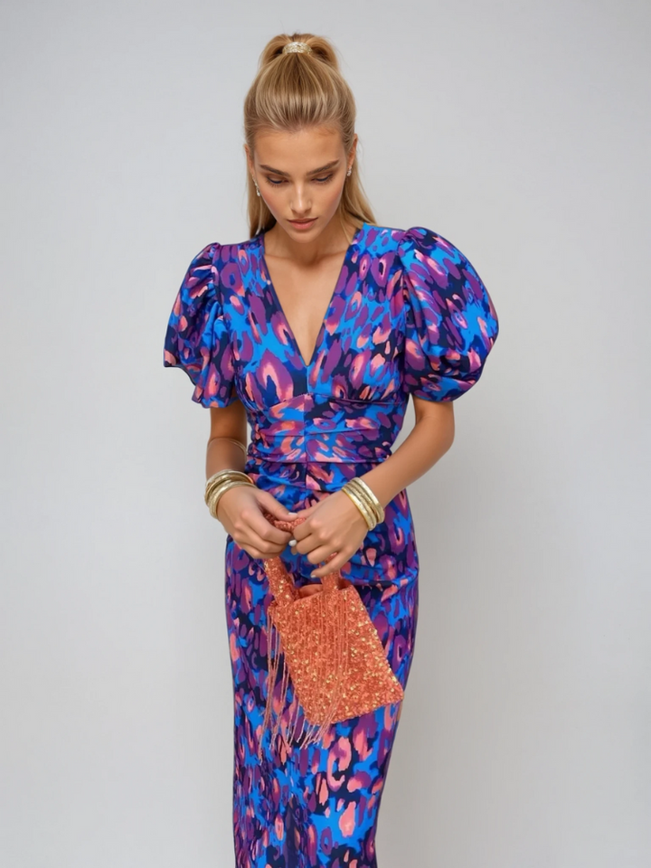 Woman wearing a colorful, patterned midi dress with puff sleeves, holding an orange fringe purse, in a studio setting.
