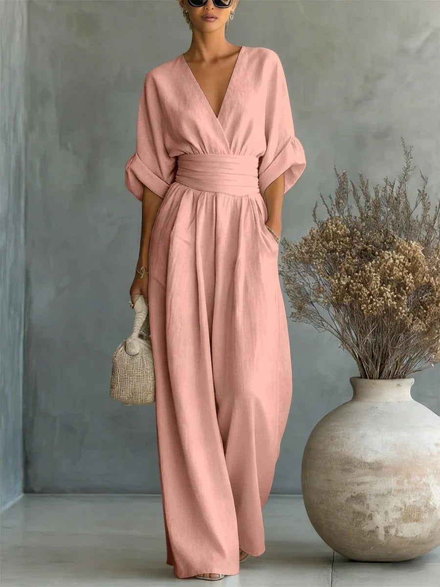 Blush pink V-neck high-waist jumpsuit with rolled-up sleeves, depicted in a studio with artistic elements and natural setting.