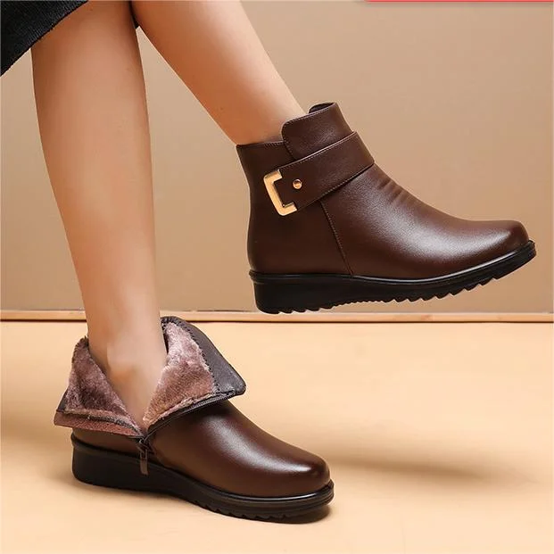 Brown ankle boots with gold buckle, one showing fuzzy lining, worn by a person, on a beige background.