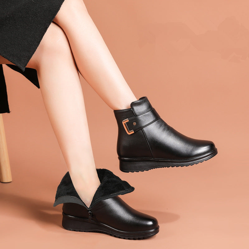 Person wearing black ankle boots with gold buckle, one showing warm lining, against a light tan background.