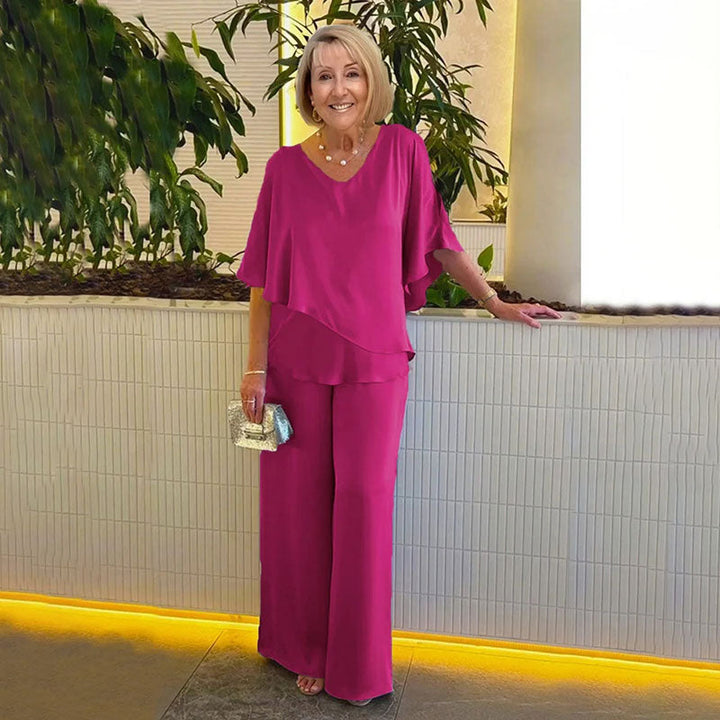 Woman in elegant magenta two-piece set, in a modern indoor setting with plants and soft lighting.