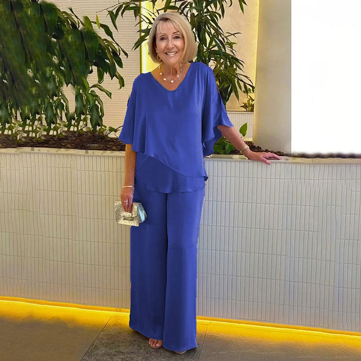 Woman in elegant blue two-piece set, in a modern indoor setting with plants and soft lighting.