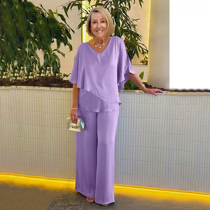 Woman in elegant lavender two-piece set, in a modern indoor setting with plants and soft lighting.