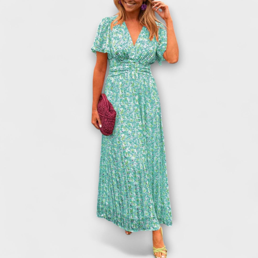 Woman in a green floral V-neck dress with short sleeves, clutching a magenta purse, on a plain background.