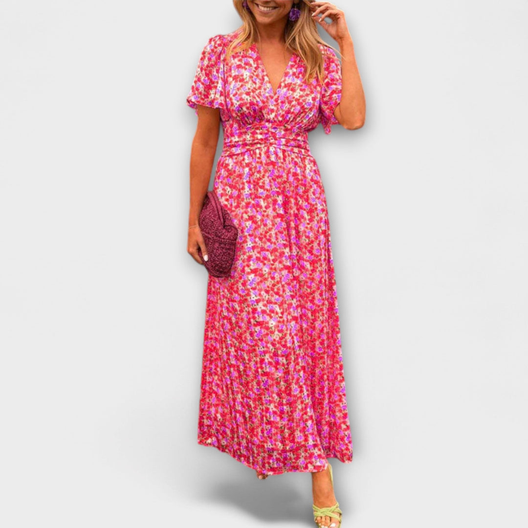 Model wearing a pink floral V-neck dress with short sleeves, holding a magenta clutch, on a plain background.