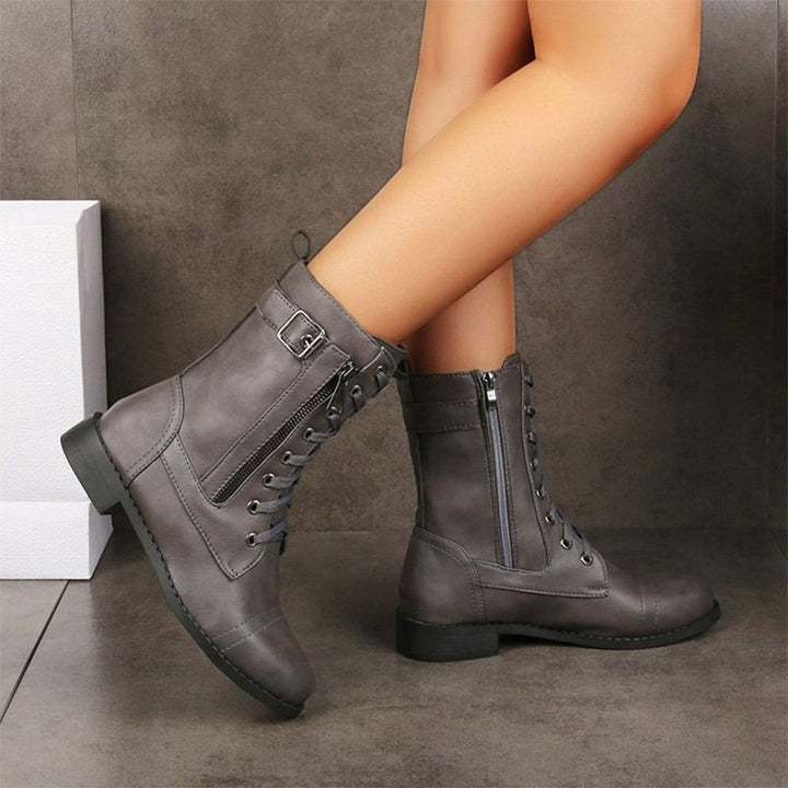 Person wearing gray round-toe boots with side zipper and lace-up design on a tiled floor.