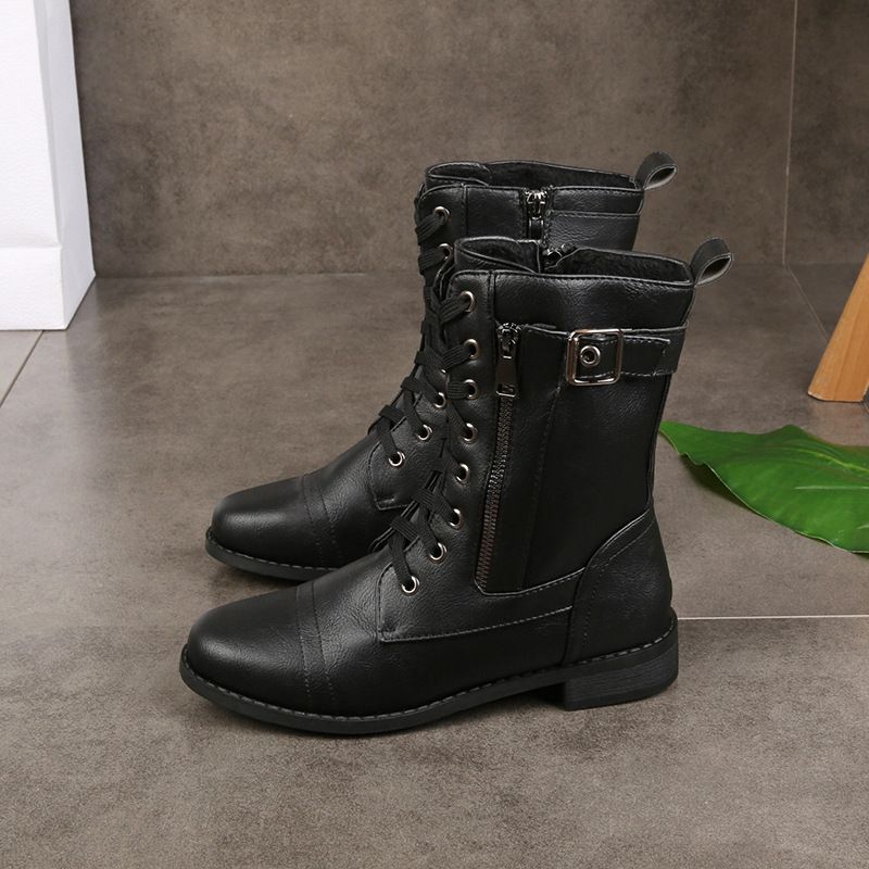 Black round-toe boots with lace-up design and zipper detail on a tiled floor with green leaf accent.