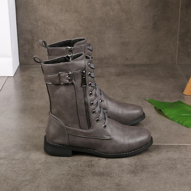 Gray round-toe boots with lace-up design and buckle detail on a tiled floor with a green leaf accent.