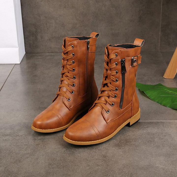Brown round-toe boots with lace-up and zipper detail on a tiled floor with a green leaf accent.