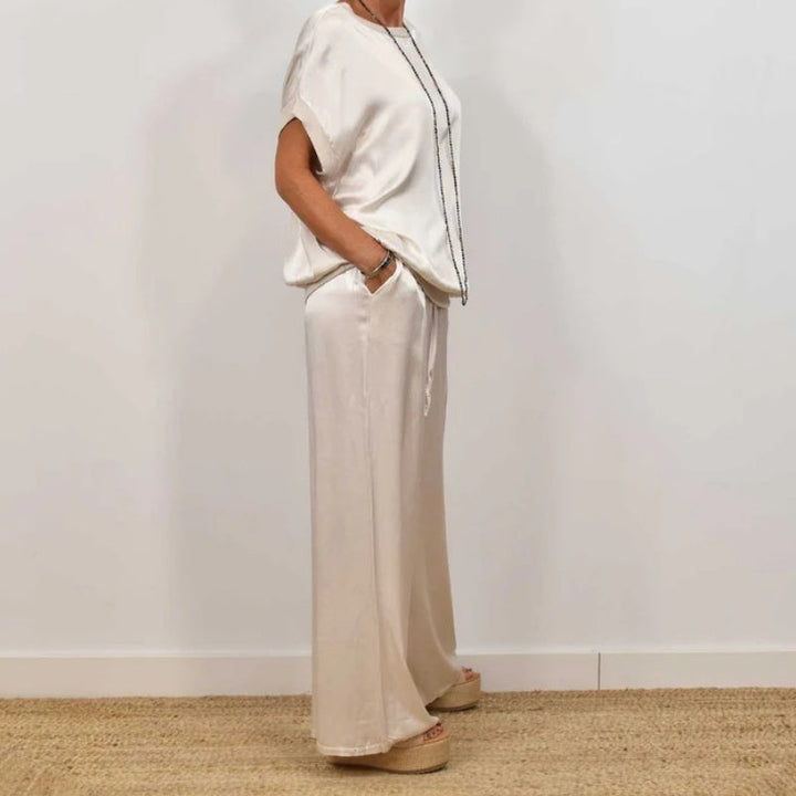 Side view of an elegant cream two-piece set with a flowy top and wide-leg pants, worn with platform sandals in a white studio.