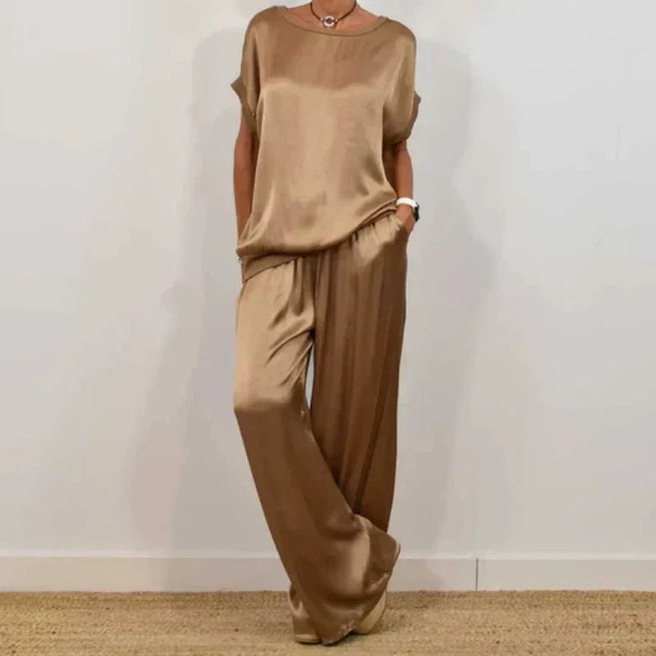 Chic beige two-piece set with a relaxed top and wide-leg pants, worn with platform sandals, in a white studio setting.