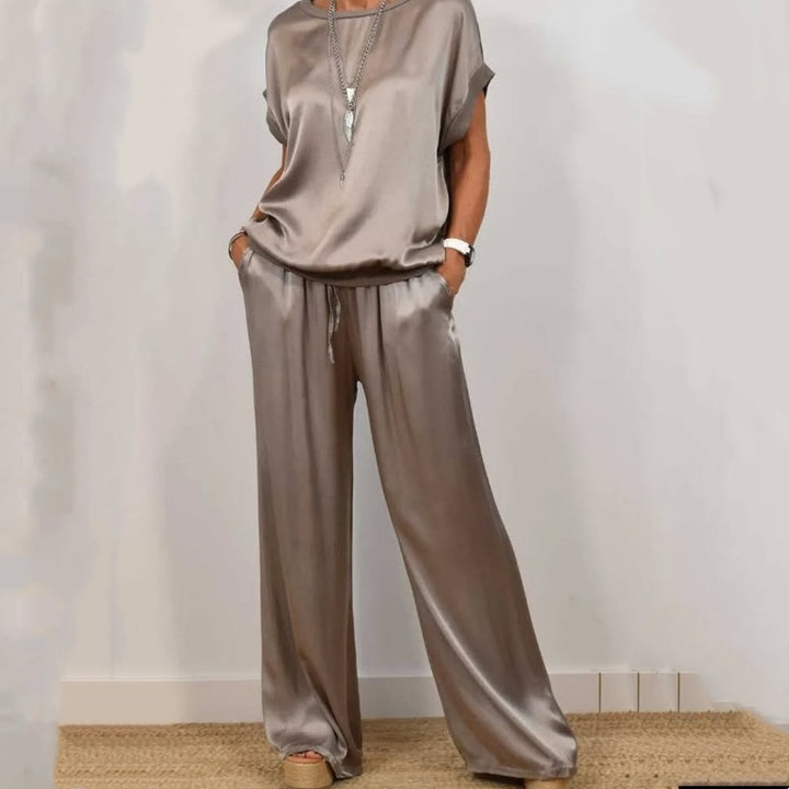 Elegant gray two-piece set with a flowy top and wide-leg pants, accessorized with a layered necklace, in a white studio.