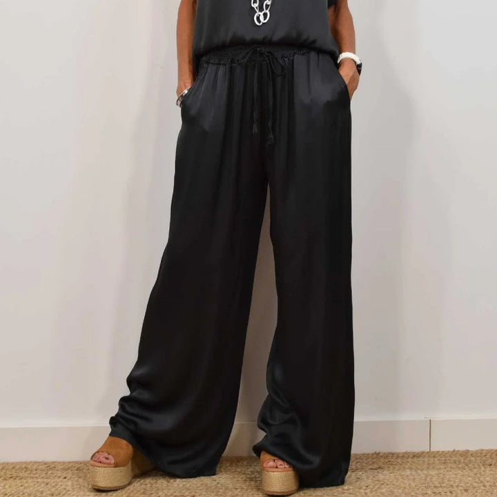 Close-up of elegant black wide-leg pants with a relaxed top, worn with platform sandals, in a white studio setting.