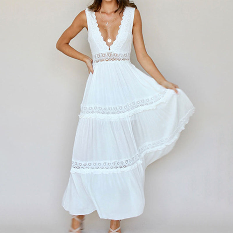 Woman in white maxi dress with lace details, deep V-neckline, against a plain studio backdrop.