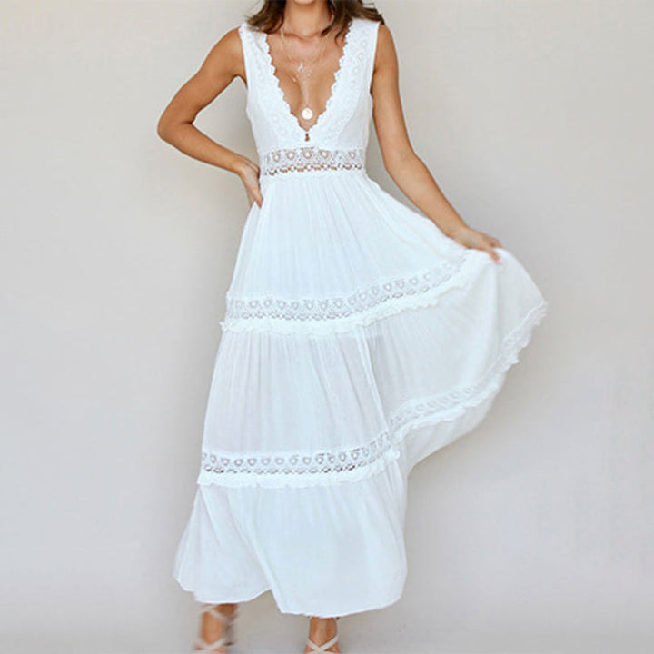 Woman in white maxi dress with lace details, deep V-neckline, against a plain studio backdrop.