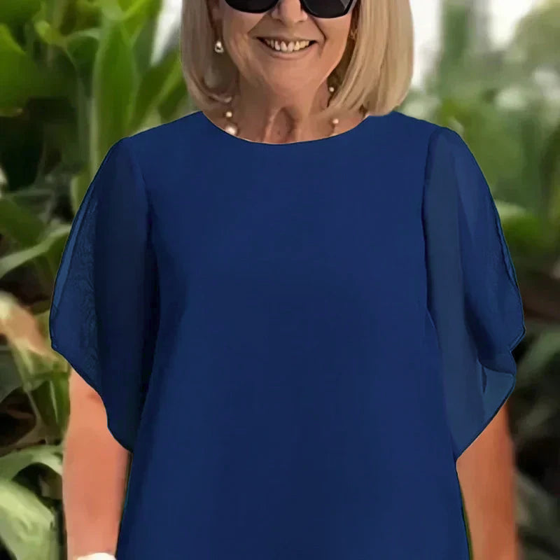 Close-up of elegant navy blue top outdoors; lush green foliage background.