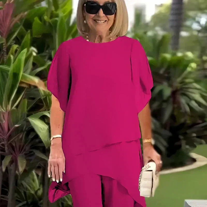 Close-up of elegant magenta top outdoors; lush green foliage background.