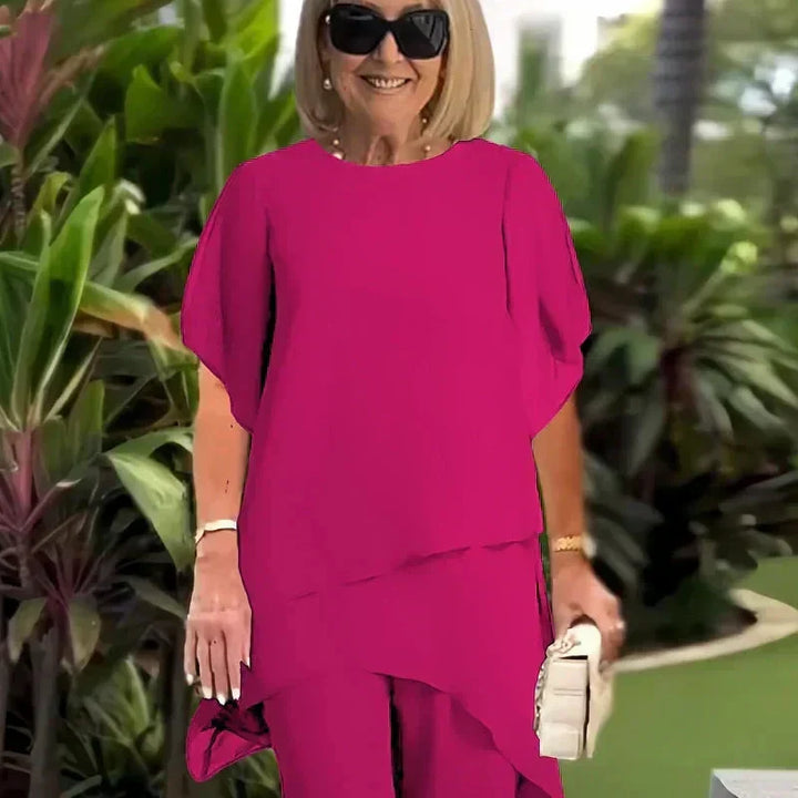 Close-up of elegant magenta top outdoors; lush green foliage background.