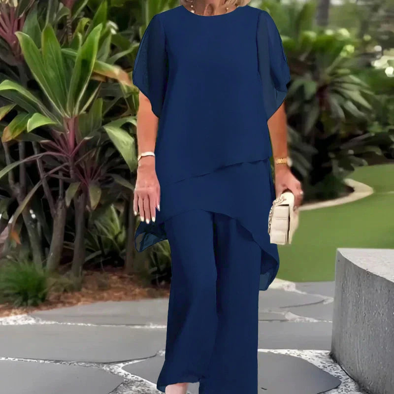 Elegant navy blue two-piece set worn outdoors; lush green foliage background.
