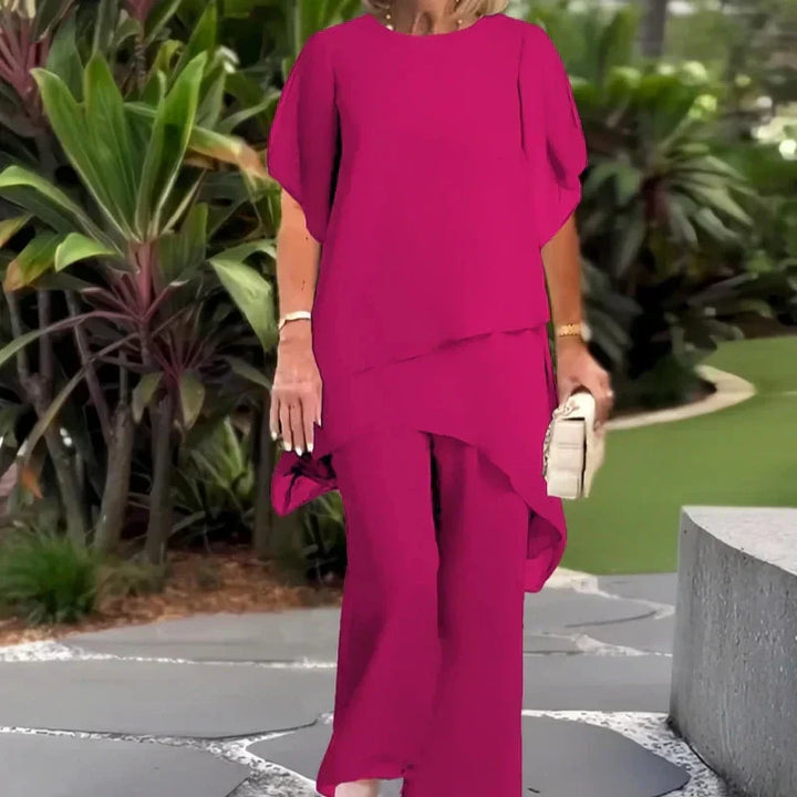 Elegant magenta two-piece set worn outdoors; lush green foliage background.